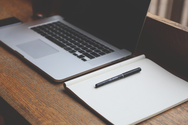 laptop on a table with paper and pen